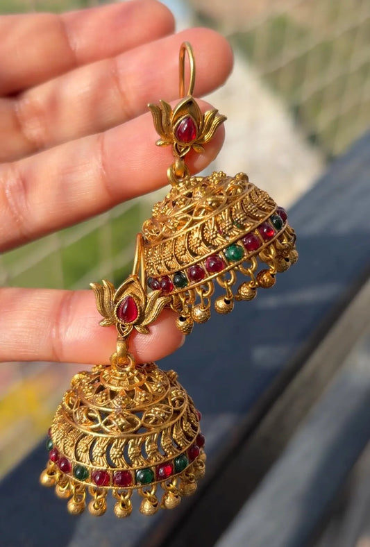 Antique gold lotus jhumka earrings with ruby-red and emerald-green stones, intricate filigree detailing, and traditional dangling bead accents.